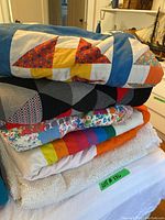 Stack of four quilts and white tufted chenille bedspread