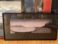Framed print with carved Haida canoe and tree line along a beach in minimalist style and muted colors.
