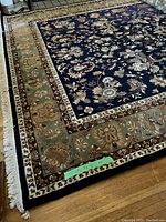 Full view of navy and green bordered Persian style rug on wood floor showing floral design and fringe