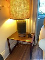 Three-quarter view of ceramic lamp on wooden side table, lamp illuminated