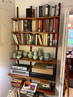 Full height view of three vertical rails with five adjustable shelves loaded with books, pottery, audio equipment.