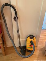 Full view of yellow Miele Solaris canister vacuum with attached hose, wand and floor nozzle on hardwood floor
