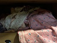 Box containing assorted fabric pieces and lace trim, highlighting a pink floral fabric and cream lace trim on top