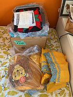 Stack of folded projects in clear plastic including red and green star quilt top, yellow floral fabric and wooden hedgehog panel visible