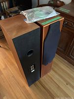 Pair of wood veneer floorstanding speakers with one grille removed showing front and side profiles
