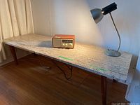 Overall view of stone coffee table with wooden legs, Sangean radio, and desk lamp