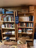 Wide view of two wooden bookshelves filled with books, magazines, and boxes in a basement room with wood panel walls.