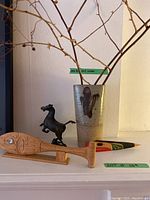 Photo showing the ceramic vase holding branches, small wooden raven figurine, wooden carved paddle lying in front