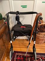 Front view of Nexus rollator walker showing seat, handles, and attached umbrella, with wooden cane and metal walking stick resting on it.