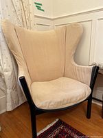 Front-left three-quarter view of wingback chair showing beige slipcover and black wooden frame
