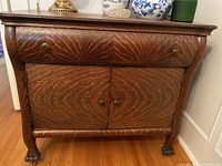 Front view of wooden cabinet showing one drawer above two doors with brass knobs and detailed wood grain pattern.