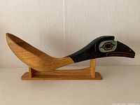 Carved wooden spoon carved with a large bird head handle, painted with indigenous design colors, placed on a wooden stand.