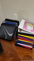 Stack of colorful hard plastic binders alongside three black Five Star zip-up binders leaning against the wall.
