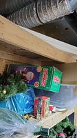 Photo of boxed Storyteller Santa figure, artificial pine branches, and some unopened holiday decoration boxes on basement shelf