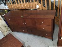Front view of dark wood dresser showing six drawers and central cabinet door with silver knobs.