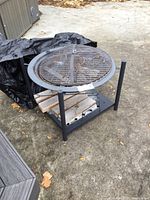 Fire pit assembled with the screen cover and metal frame visible on an outdoor surface alongside a black cover.