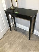 Front view of the small black hall table showing the single drawer and tapered legs.