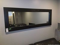 Large rectangular mirror hung on wall showing full front view with black wooden frame.