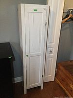 Front view of tall narrow white pantry cabinet showing bubbling on door and round knob.