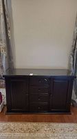 Front view of dark wood sideboard with central drawers and side cupboards, glass top in place