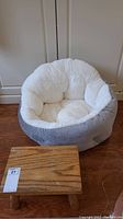 Plush beige and grey pet bed with small wooden step stool in front, showing dimensions and general condition.