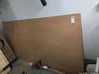 Photo showing stacked plywood sheets leaning against a wall with a tool on the floor nearby.