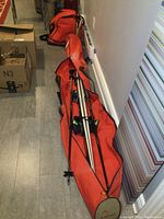 Orange ski storage bag holding a pair of white Dynastar skis and black ski poles stored inside the bag.