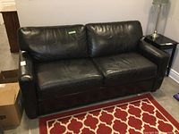 Front view of black leather sofabed showing two-seat cushions, armrests, and overall condition with visible wear.