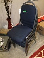 Stacked set of four blue fabric chairs with metal frames, side angle showing stacking feature and chair dimensions around 18x36 inches.