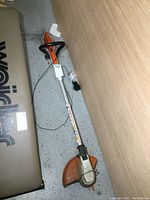 Full view of Stihl cordless trimmer showing shaft, handle, and cutting head on floor.