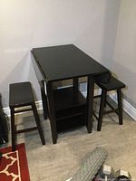 View of drop-leaf table with stools, showing closed leaves and shelves in base