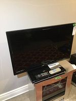 Funai 32-inch flat screen TV sitting on a wooden stand with Toshiba DVD player and two remotes on top