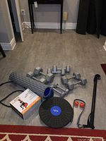Photo showing cast iron dumbbells of various weights, large gray foam roller, balance board, resistance cord, and a boxed exercise ball.