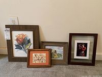 Four framed art pieces displayed against the wall on the floor, showing various flower and bird artworks along with lady with goldfish bowl photo.