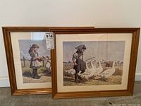 Pair of framed art prints leaning against a white wall, showing two girls on a farm with white ducks, framed in brown wood and white matting.