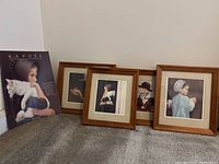 Four framed mini art prints resting against the wall on gray carpet, showing portraits of children, each framed in simple brown wood frames.