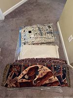 Folded bedspreads and hunting blanket displayed on floor; blanket with hunting dogs and birds shown at front with fringe detail.