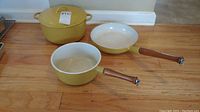 Three yellow enamelware cookware pieces from Descoware: large Dutch oven, saucepan, frying pan with wood handles on saucepan and frying pan