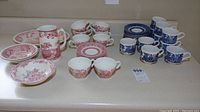 View of entire dish set including pink scenic plates, cups, and blue floral cups and saucers