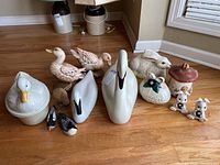 Full lot arranged on floor including mushroom lidded box, bunny figurines, two white plastic swans, ceramic and wooden ducks, bird figurine, and duck on nest canister.