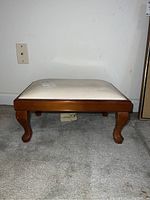 Side view of footstool showing wooden curved legs and upholstered top.