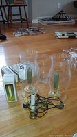 Photo showing three clear hurricane glass candle holders each with a green taper wax candle inside, two electric candles with attached wiring, and boxed items.