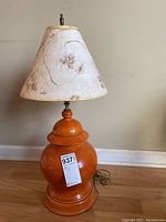 Full view of the lamp showing the textured white fabric lampshade with floral details and the orange ceramic base with rounded shapes and tiers.