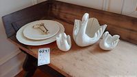 Complete lot showing Lenox swan trio, two feather-pattern plates, and metal assembly pieces on a wooden table.