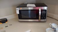 Front view of Hamilton Beach stainless steel microwave with owner's manual on top