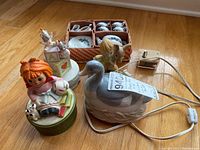 Four music boxes, one duck lamp, and a boxed miniature china set arranged on wood floor