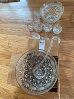 Top-down view of one punch bowl with textured starburst pattern and glass ladle resting inside, along with several small punch cups around it.