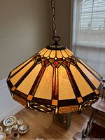 Front angle view of a Dale Tiffany stained glass hanging light fixture with amber and reddish stained glass panels and dark leading.