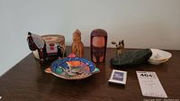 Overview of lot on table showing carved wooden figurines, ceramic dish, trinket holder, and small decorative items