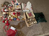 Overview of assorted Christmas decorations on floor: boxes of ornaments, figurines, ribbon, garland and tree stand